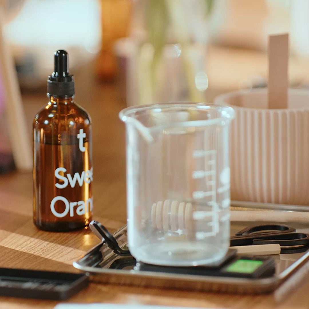 Bottle labeled 'Sweet Orange' on a wooden table with a candle and other items.