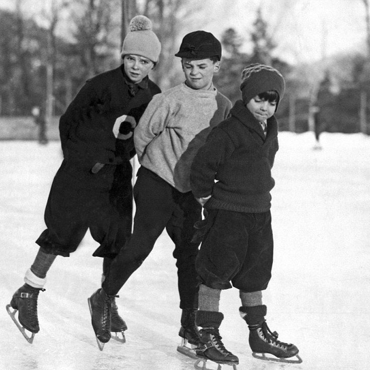 Three people ice skating outdoors on a frozen lake, with trees in the background.